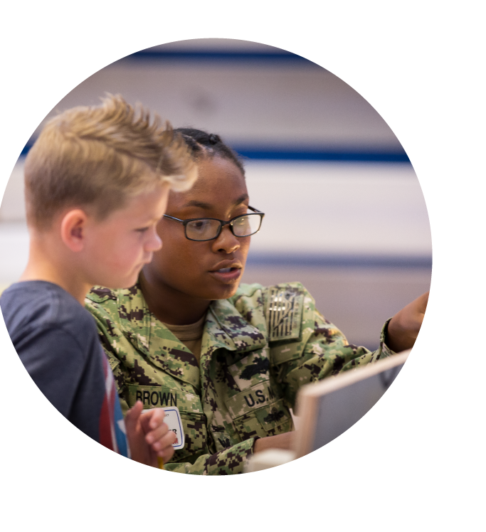 A military woman in uniform with a young boy, both focused on a task.