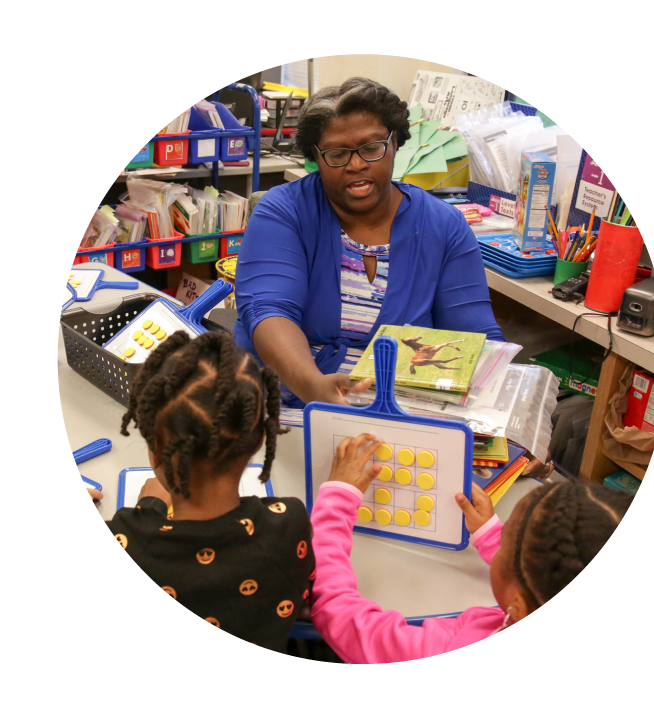 A teacher with two young students in a classroom setting.